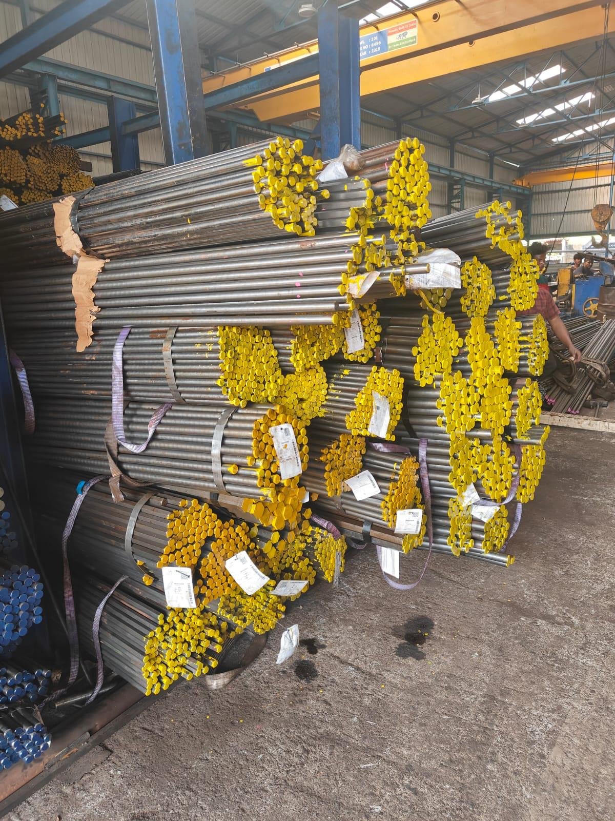 Bundles of bright bars with yellow grade-marked ends stacked under the overhead crane at Radhe Steel, Bhosari, Pune